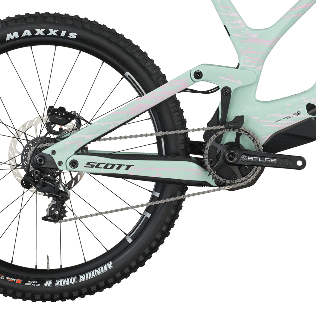 High-performance Scott Gambler DH bike with dual crown fork and coil shock, photographed on a rocky overlook with sweeping views of green hills and a distant village.