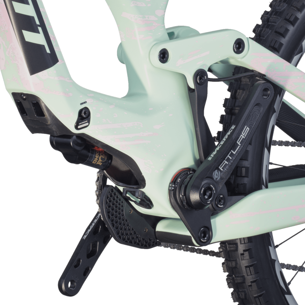 Scott Gambler carbon downhill bike with Fox suspension and wide tires, standing on a rock ledge overlooking a lush valley under a bright summer sky.